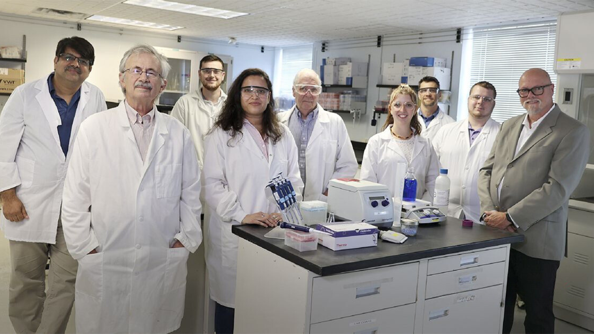 A team of scientists in lab coats gathered around lab equipment, representing a collaborative genetic engineering services group.