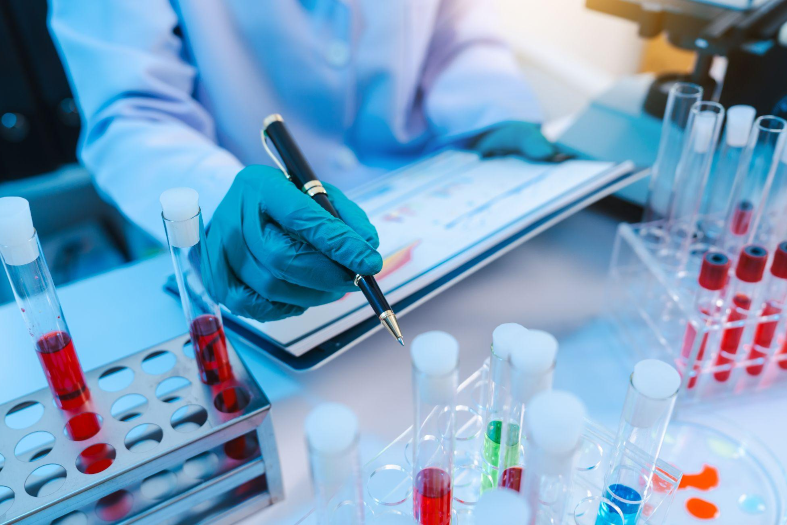 A scientist with gloves on holding a pen near test tubes