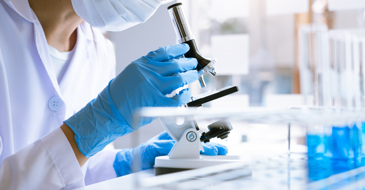 A scientist looking at a substance underneath a magnifying glass