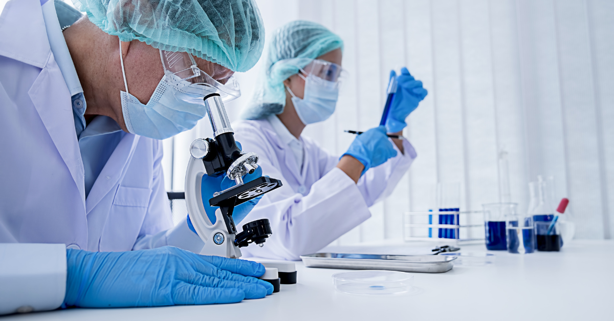 Two scientists wearing masks and gloves looking at substances under microscopes