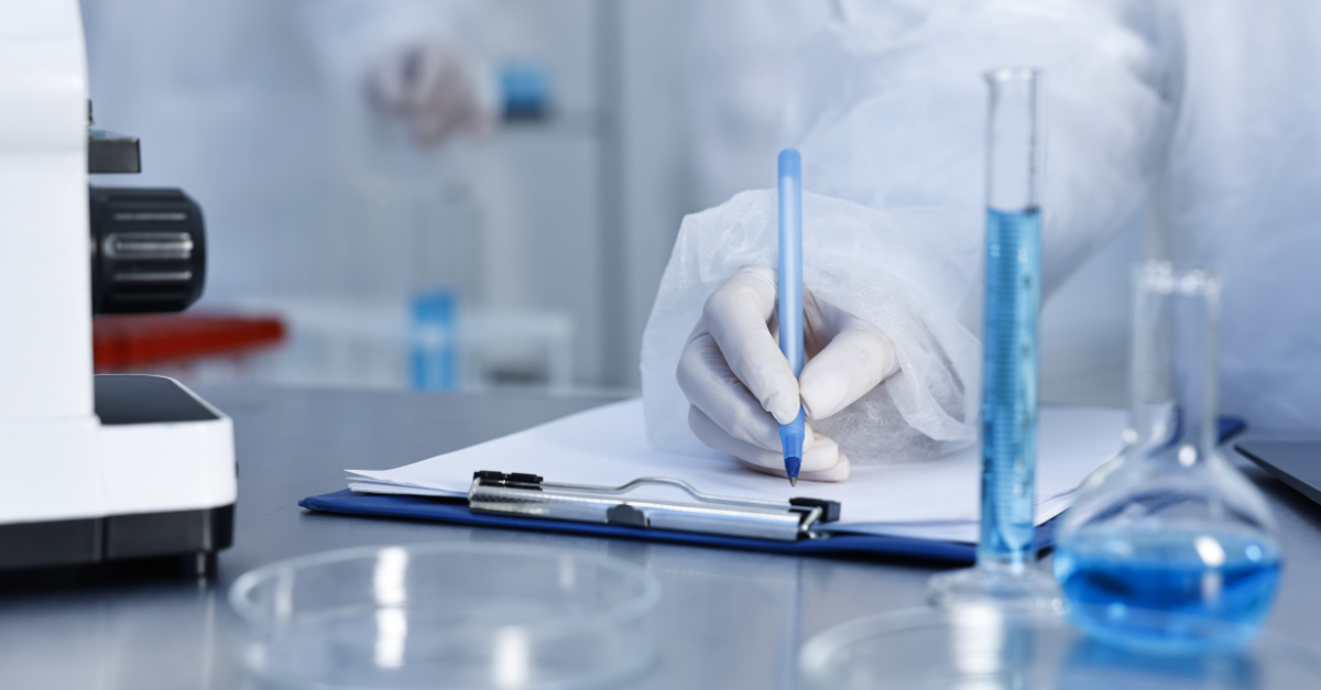 A scientist wearing gloves writing on a clipboard