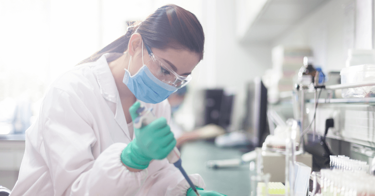 A masked scientist carefully expels a sample