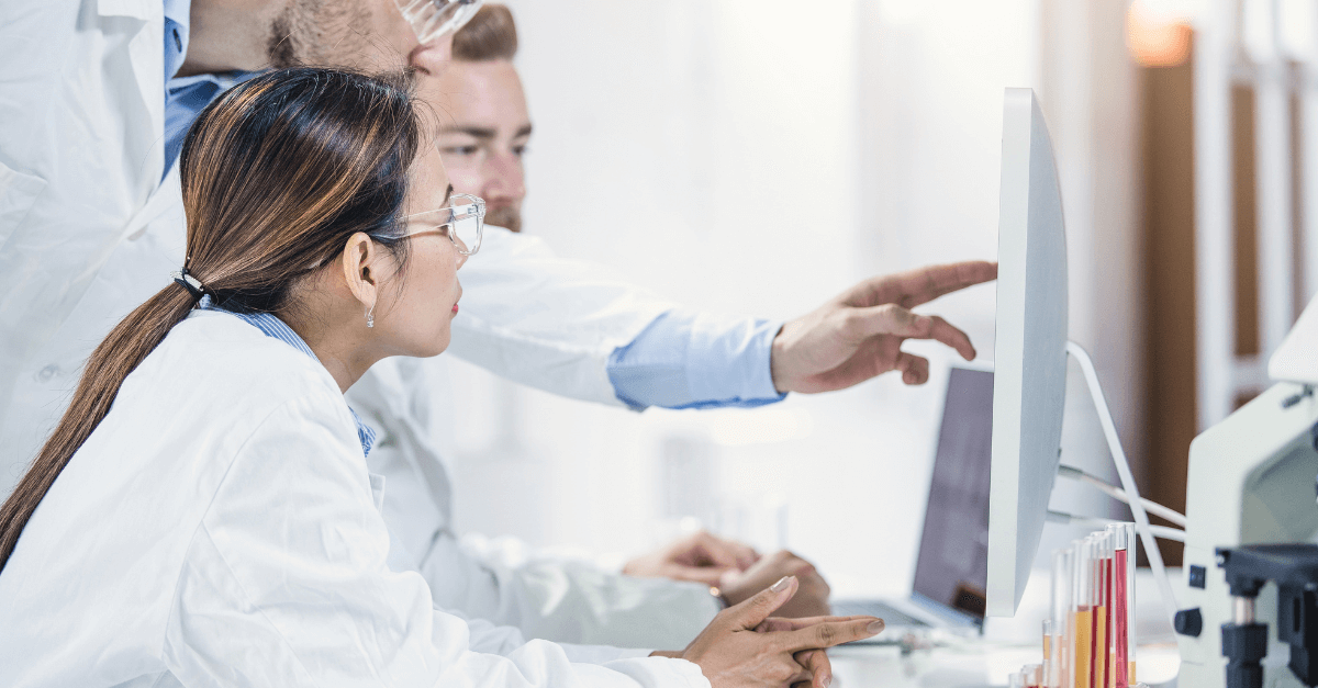 A group of scientists peer over a computer monitor pointing at it
